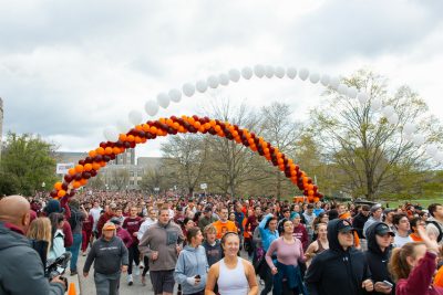 Runners cross the start line beneath an arch of orange and maroon balloons.